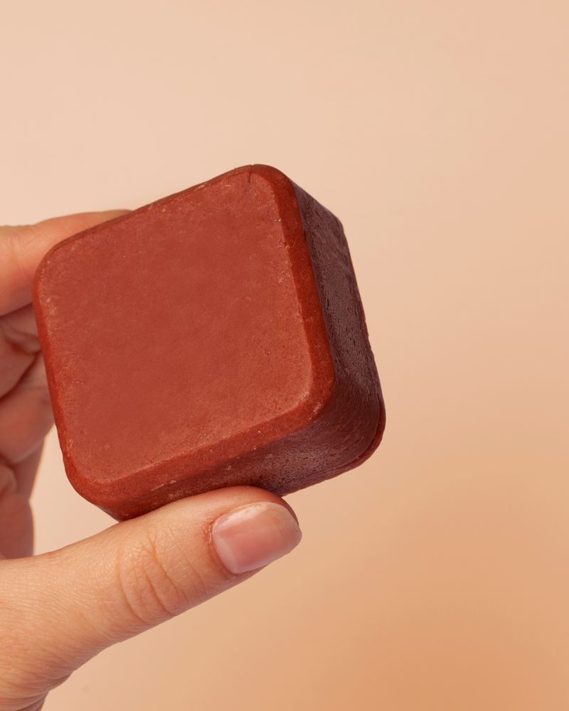 Mano che tiene una gemma di shampoo solido Ristrutturante Enooso al melograno
